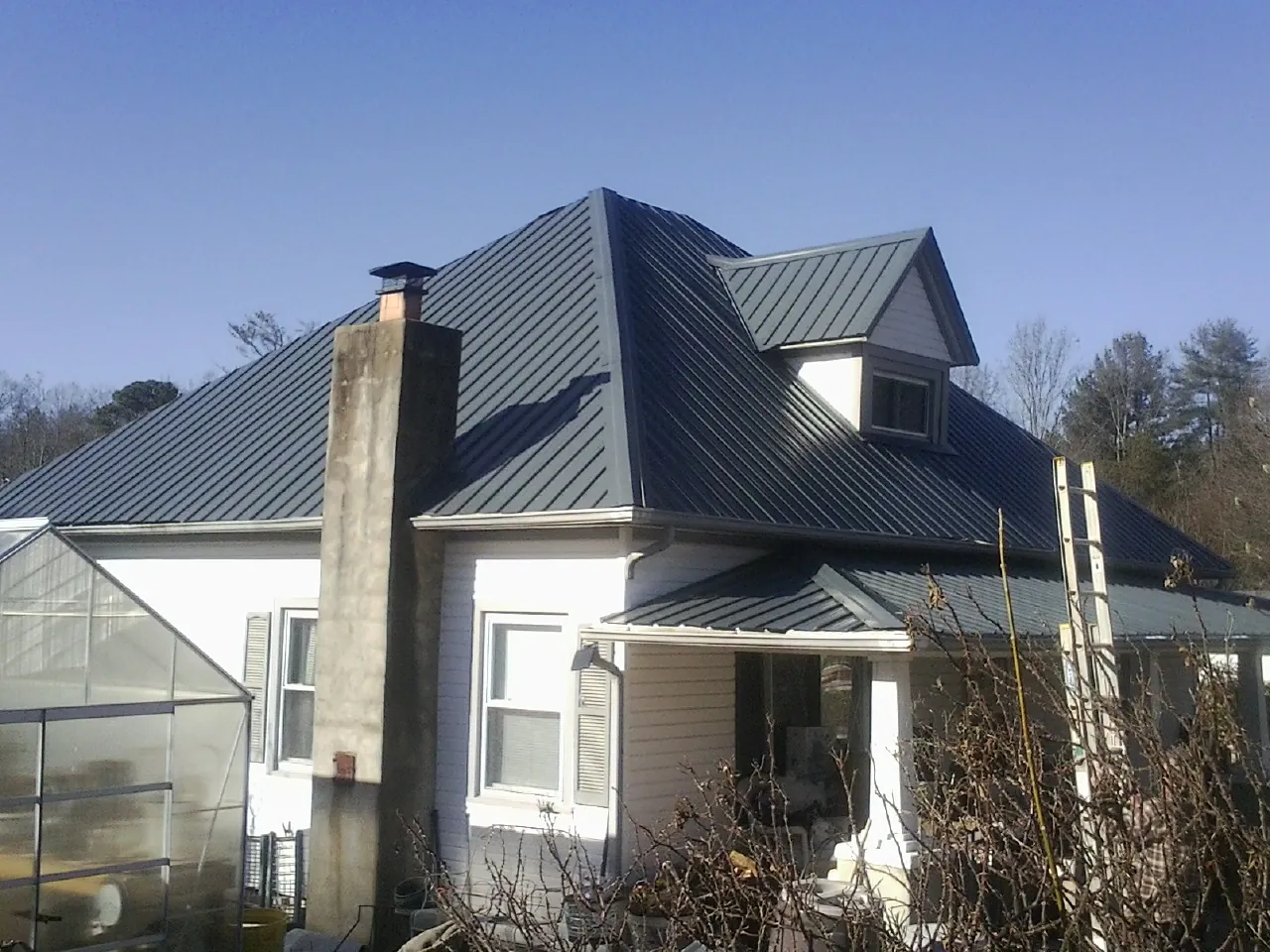 Dark blue standing seam metal roof on a white farmhouse with dormer — Slate & Tile Roof Repair by Roofing Brothers in Woodbine