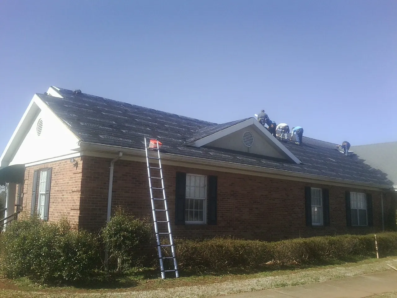Crew tearing shingles off a brick ranch roof with a ladder set — Metal Roof Repair work by our crew in Woodbine