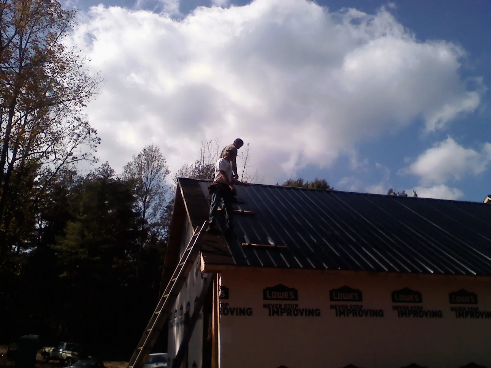 Roofer fastening dark metal panels high against a cloudy sky, from a Roof Inspection job in Woodbine